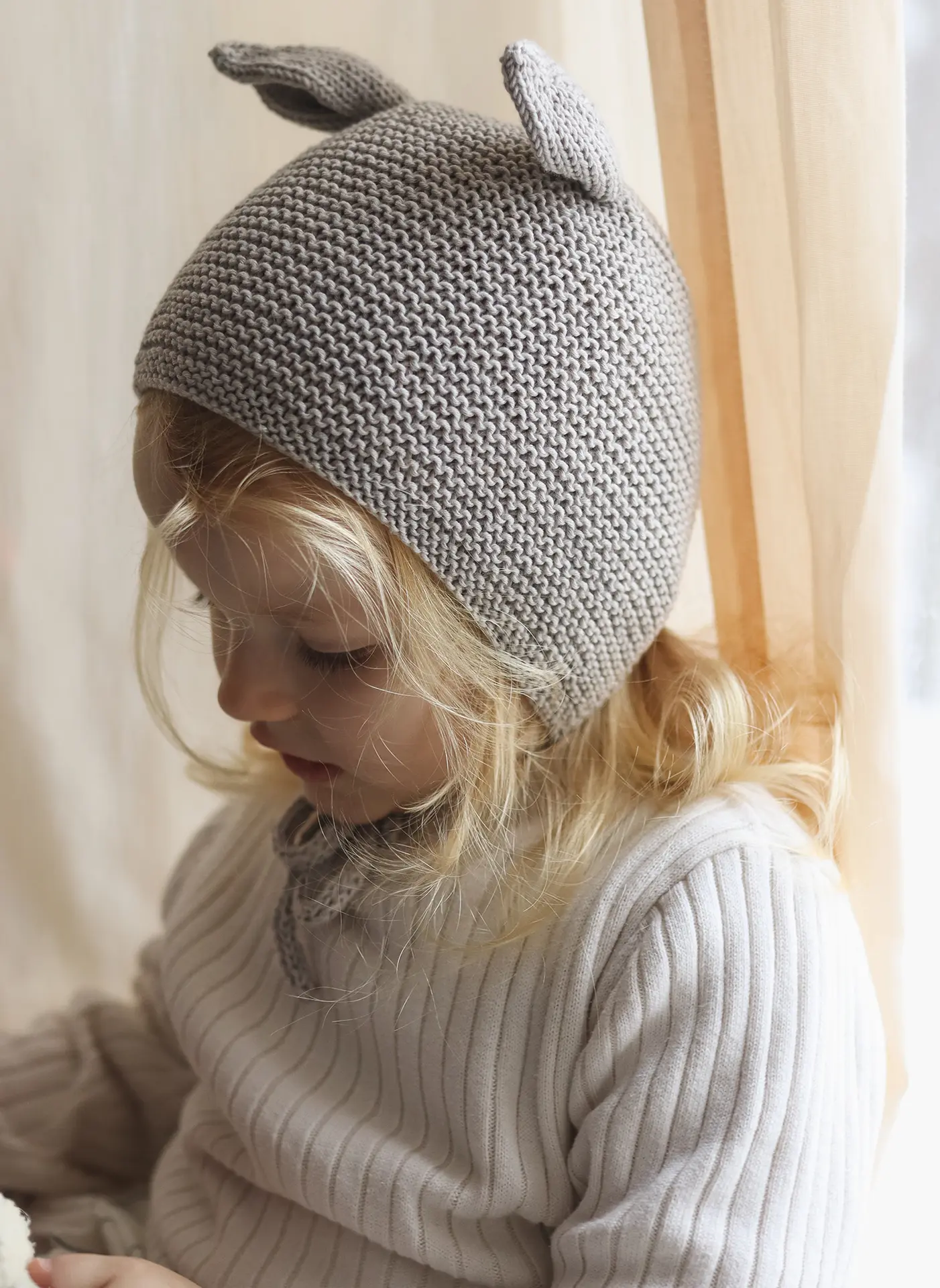 Smal girl wearing hand knitted hat with animal ears in gray color