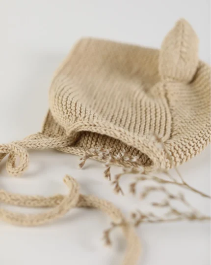 A handmade hat with pointed ears in a delicate warm beige color displayed on a side.